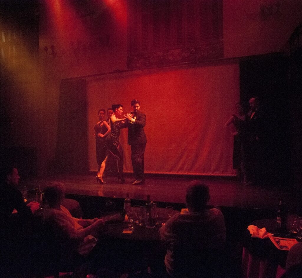 Coppia di ballerini di tango su un palco illuminato davanti al pubblico ai tavoli, metafora della pianificazione del marketing per stagioni