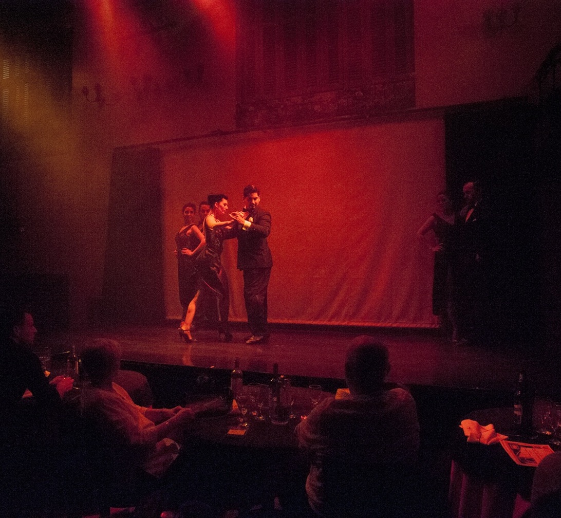 Coppia di ballerini di tango su un palco illuminato davanti al pubblico ai tavoli, metafora della pianificazione del marketing per stagioni
